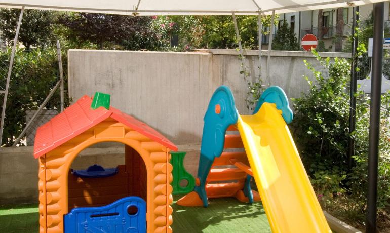 Area giochi per bambini con scivolo e casetta sotto un ombrellone.