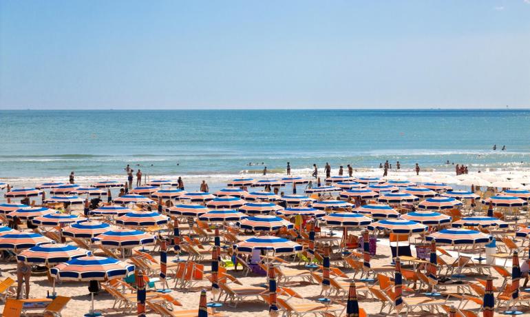 Spiaggia affollata con ombrelloni colorati e mare calmo.