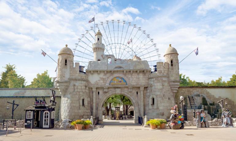 Ingresso di un parco divertimenti con ruota panoramica e castello.